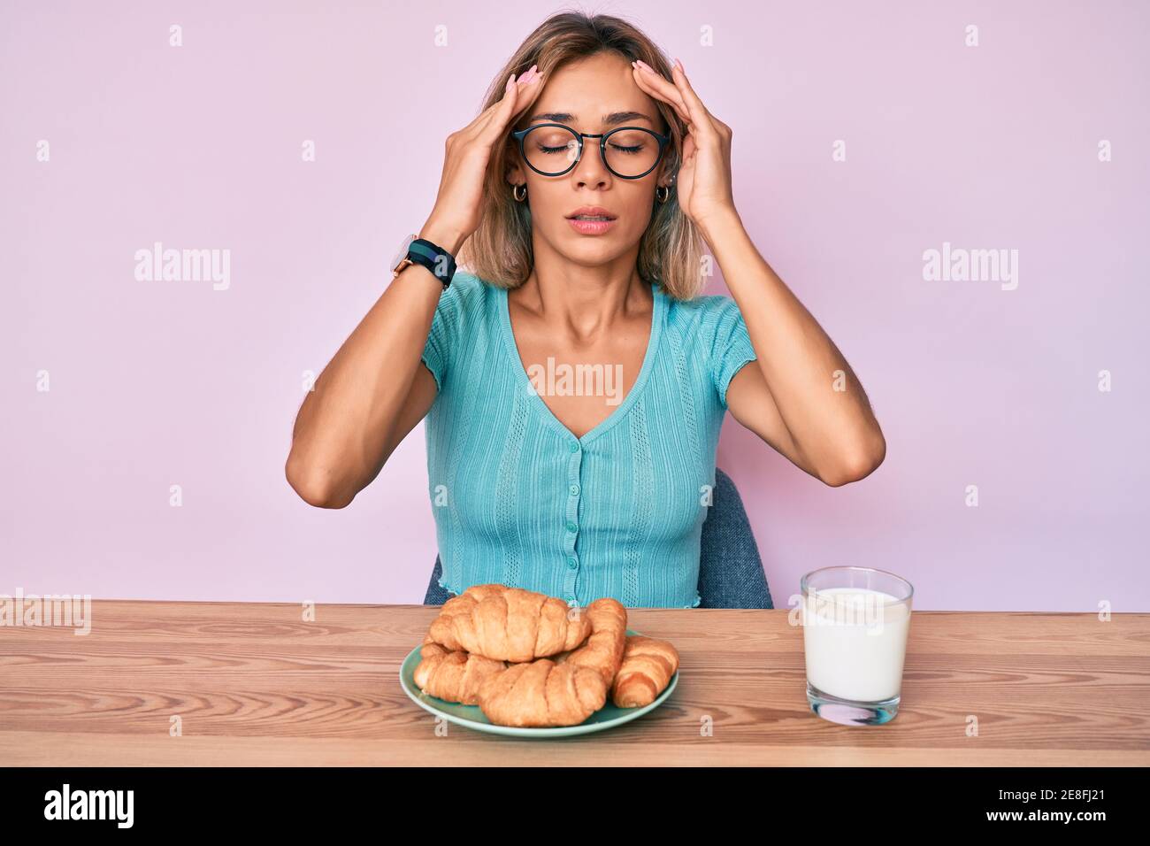 Beautiful caucasian woman eating croissant for breakfast with hand on head, headache because stress. suffering migraine. Stock Photo