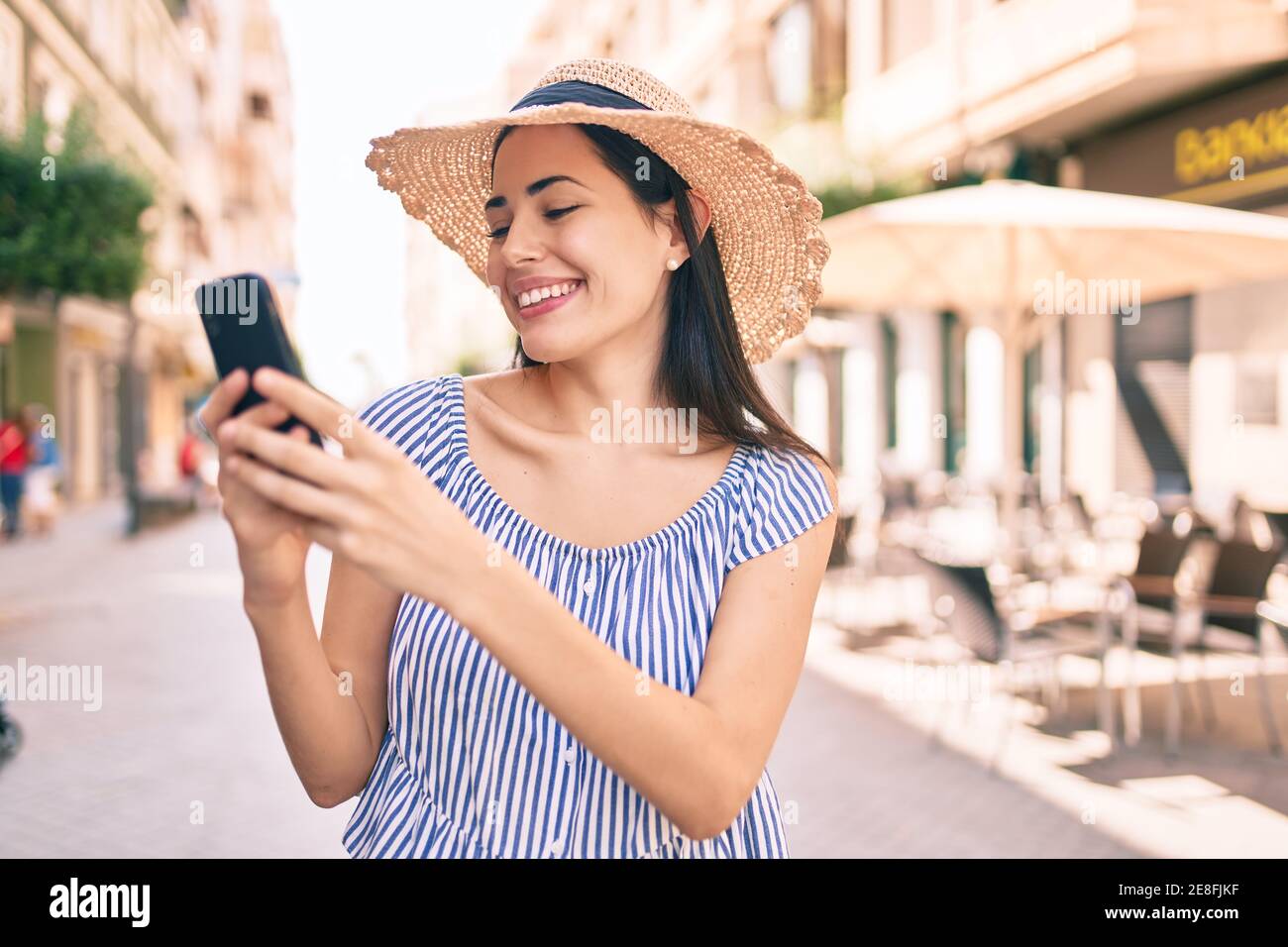 Young latin tourist girl on vacation smiling happy using smartphone at ...