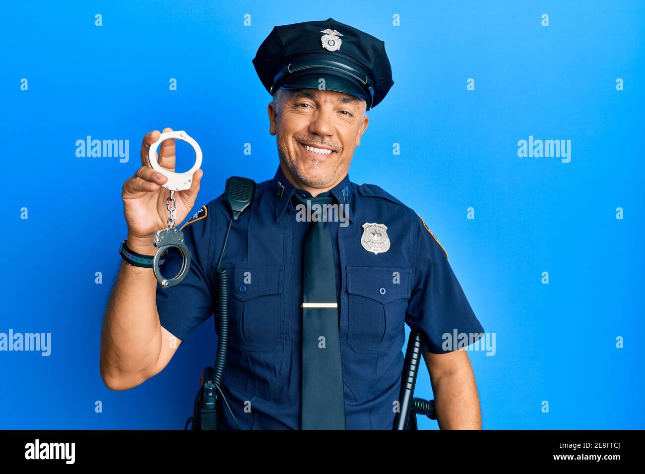 Handsome middle age mature man wearing police uniform holding metal handcuffs looking positive and happy standing and smiling with a confident smile s Stock Photo