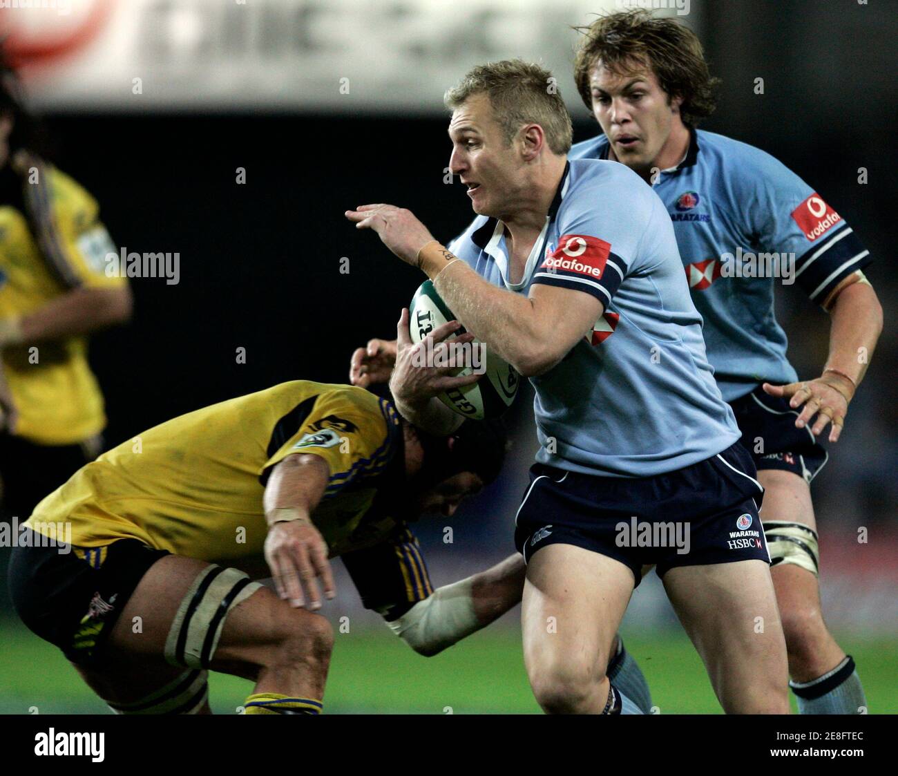 Peter Hewat (C) of the Waratahs from New South Wales is tackled by Luke Andrews (L) of the Hurricanes from New Zealand as team mate Stephen Hoiles (R) backs up during their Super 14 ruby match in Sydney May 13, 2006. The Hurricanes won 19-14. REUTERS/Will Burgess Stock Photo