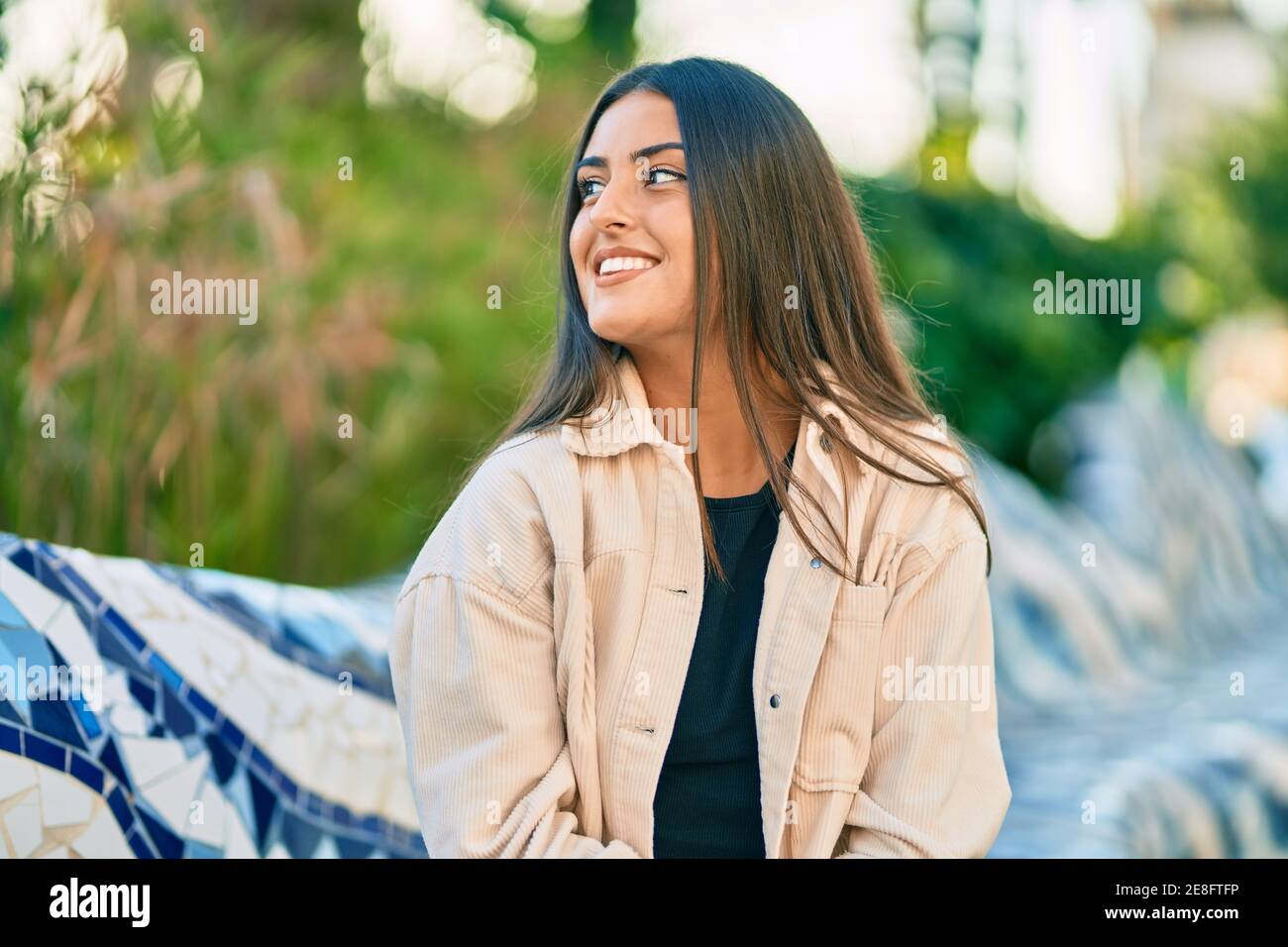 Young hispanic girl smiling happy sitting on the bench at the park ...