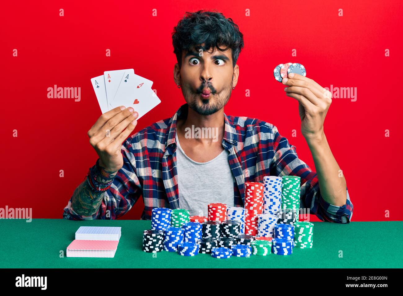 Young hispanic man playing poker holding cards and casino chips making fish  face with mouth and squinting eyes, crazy and comical Stock Photo - Alamy