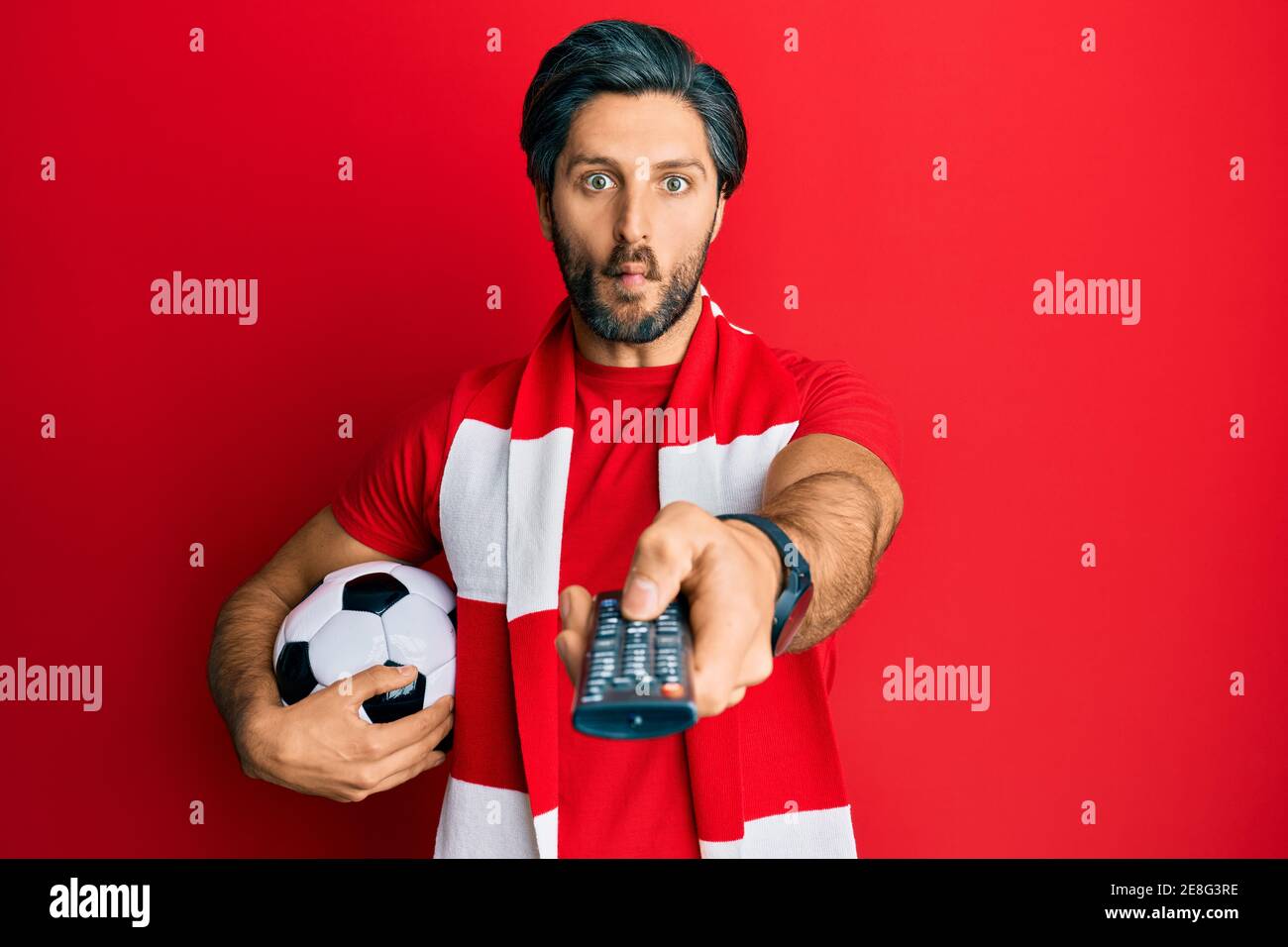 Young hispanic man football hooligan holding ball using tv control ...