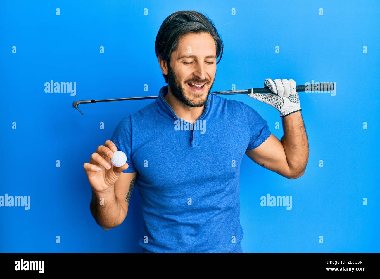 Young hispanic man holding golf ball smiling and laughing hard out loud