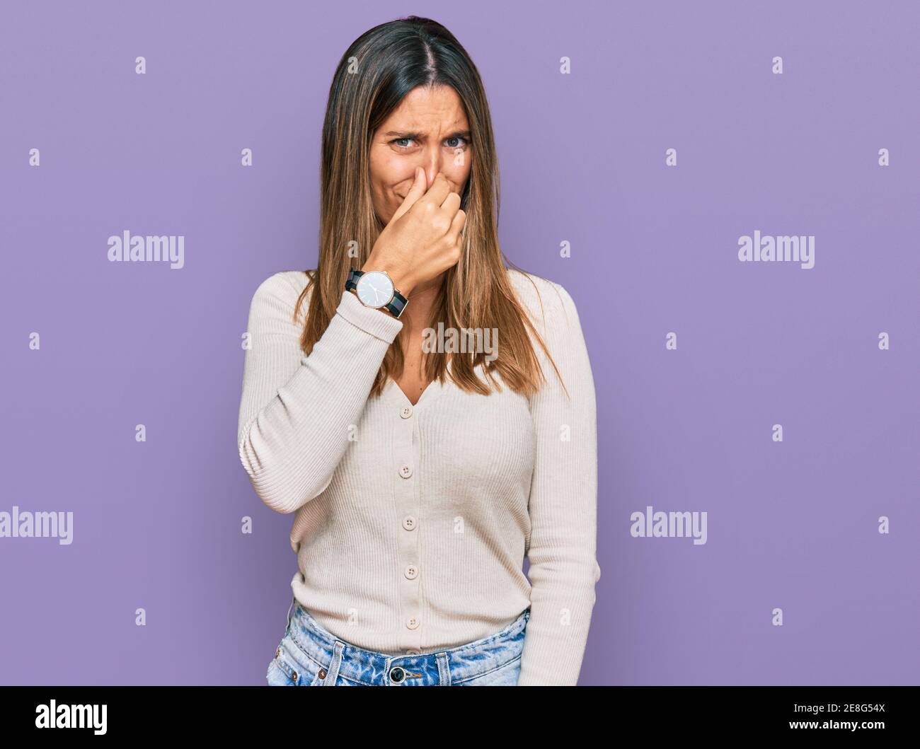 Young woman wearing casual clothes smelling something stinky and ...