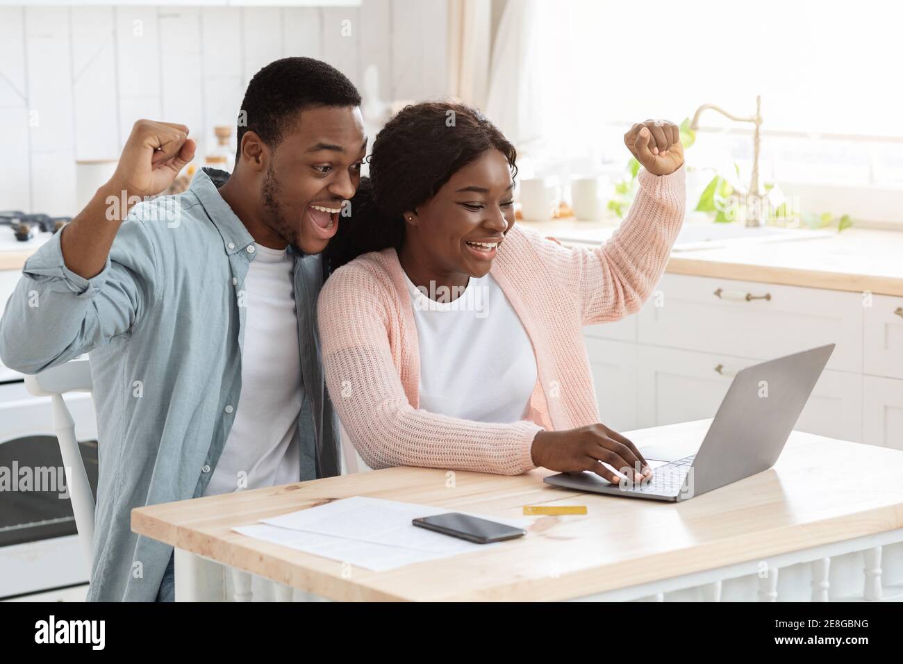 Lucky Winners. Excited african american couple with laptop in kitchen celebrating success Stock Photo