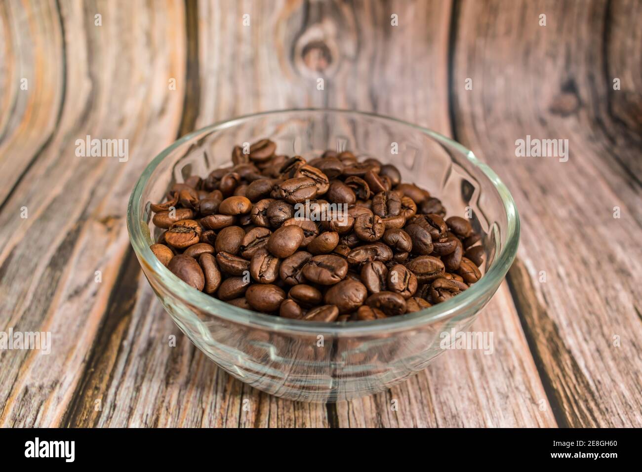 Freshly roasted coffee beans lie in a transparent glass vase on a wooden table Stock Photo