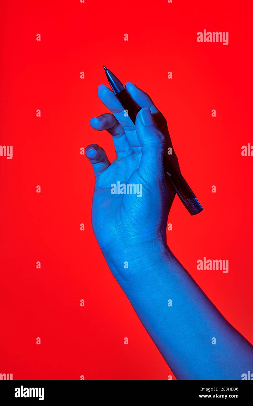 Woman's blue hand over red background, writing with a pen. Isolated