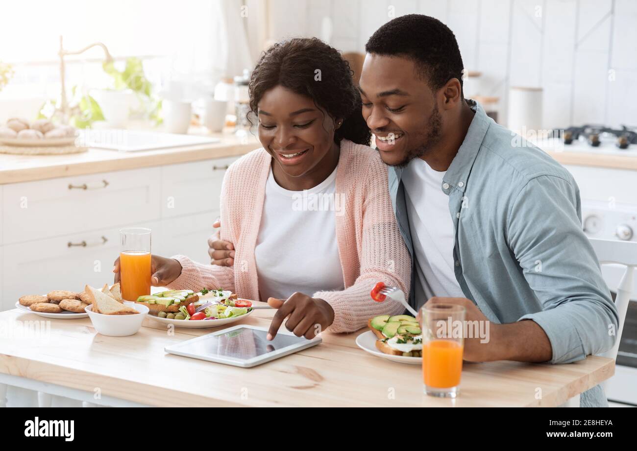 Happy Black Couple Using Digital Tablet While Having Breakfast In Kitchen Stock Photo