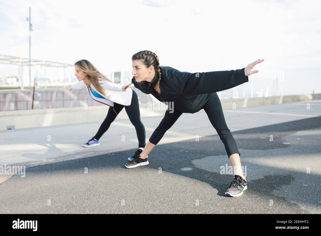 Full body fit young females in activewear bending forward on road while warming up before intense working out Stock Photo