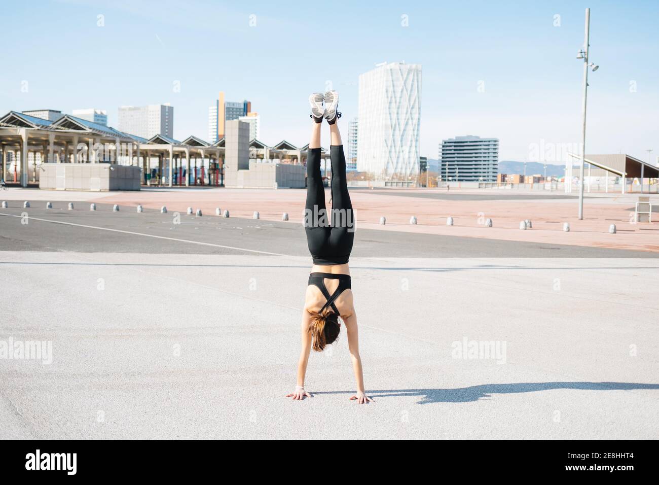 Back view full length fit determined sportsWoman in tight activewear doing handstand exercise on asphalt road on sunny suburb Stock Photo