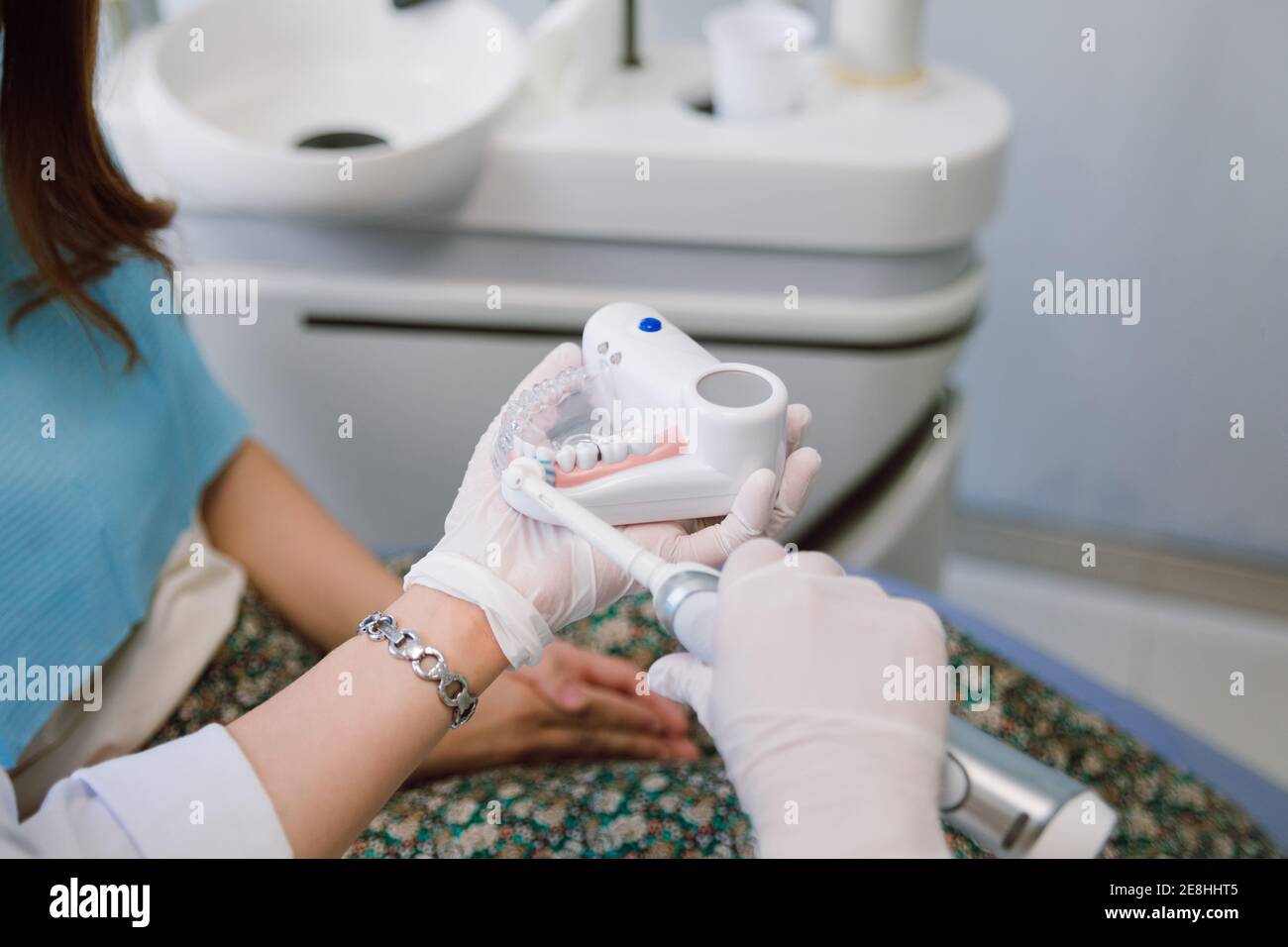 Crop unrecognizable female dental hygienist with prosthetics and electric toothbrush demonstrating patient how to brush teeth correctly during appoint Stock Photo
