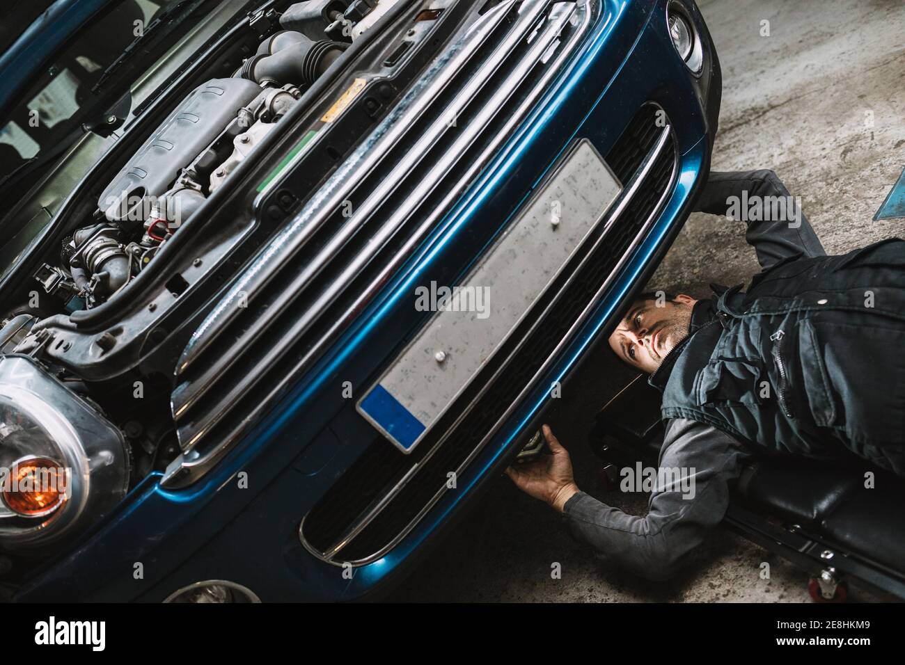 Young focused auto service man checking up vehicle with open bonnet while  lying on mat in workshop Stock Photo - Alamy