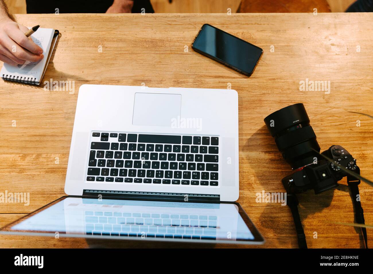 From above of crop male baristas sitting at wooden counter in coffee shop and working together while using laptop and taking notes in notebook Stock Photo