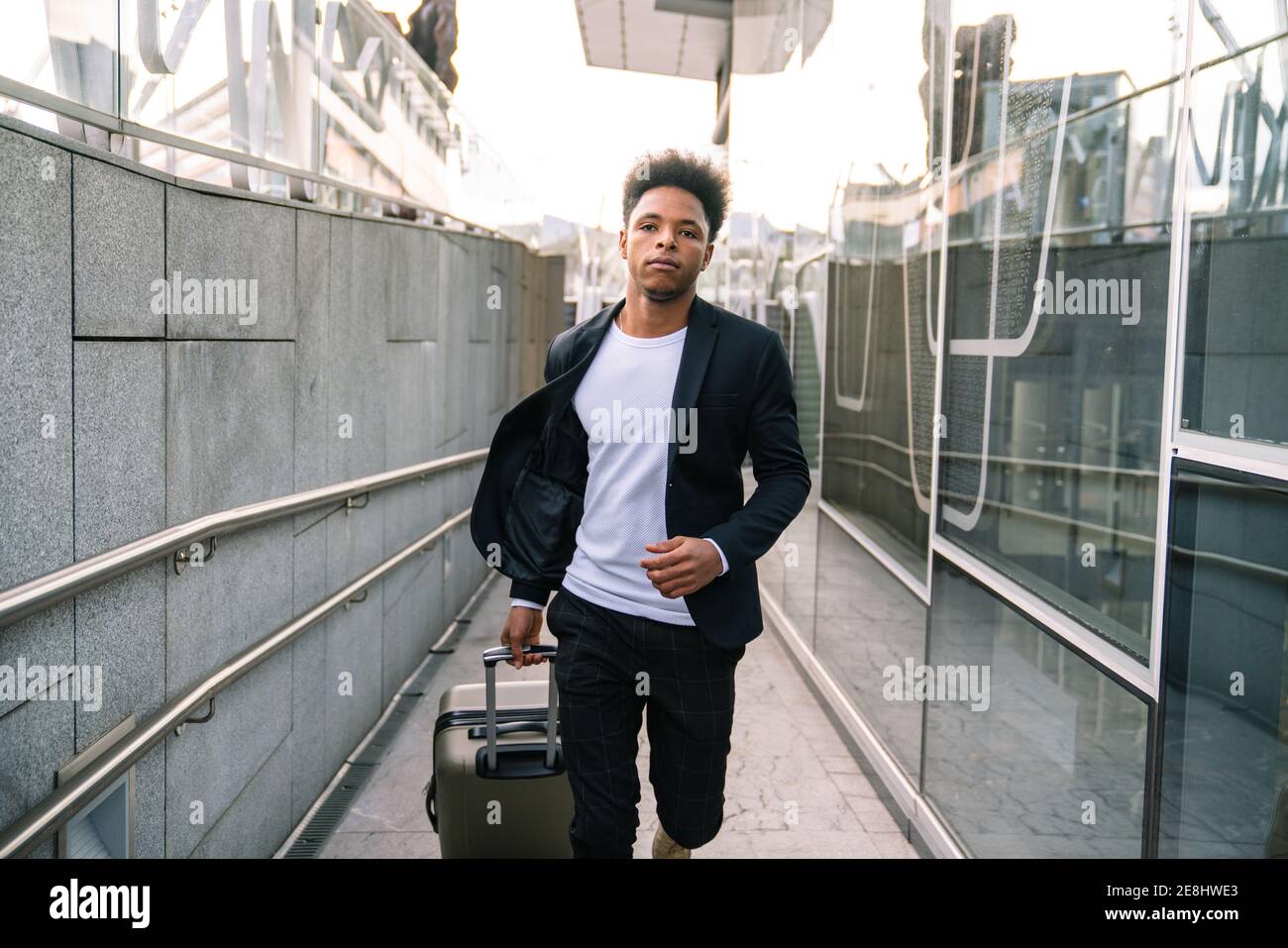 African American male tourist with suitcase running in airport while hurrying for flight and looking forward Stock Photo