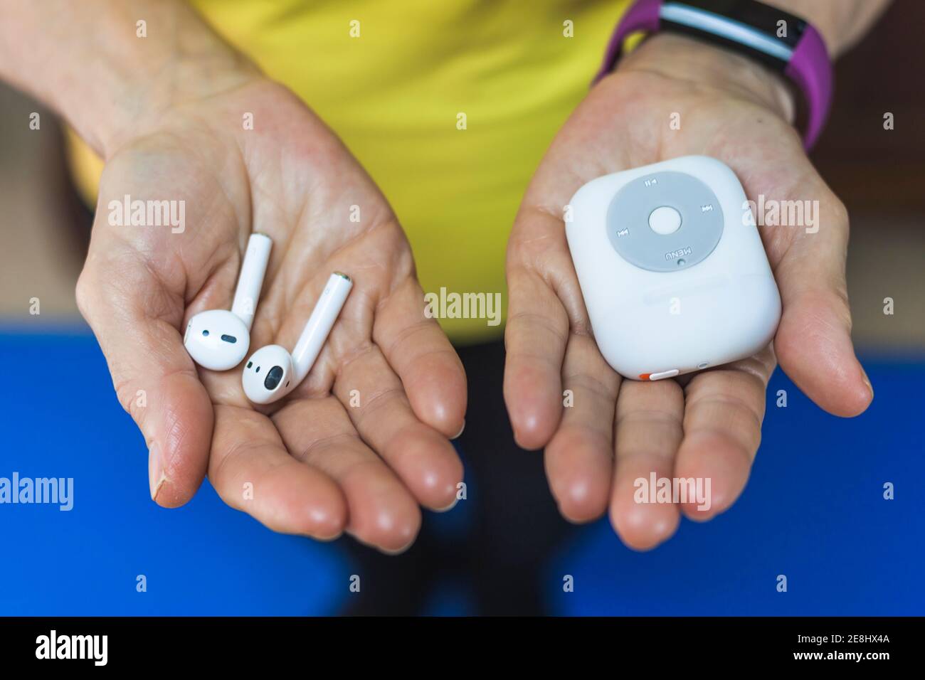 From above crop unrecognizable person wearing fitness bracelet showing wireless earbuds and modern mp3 player on hands Stock Photo