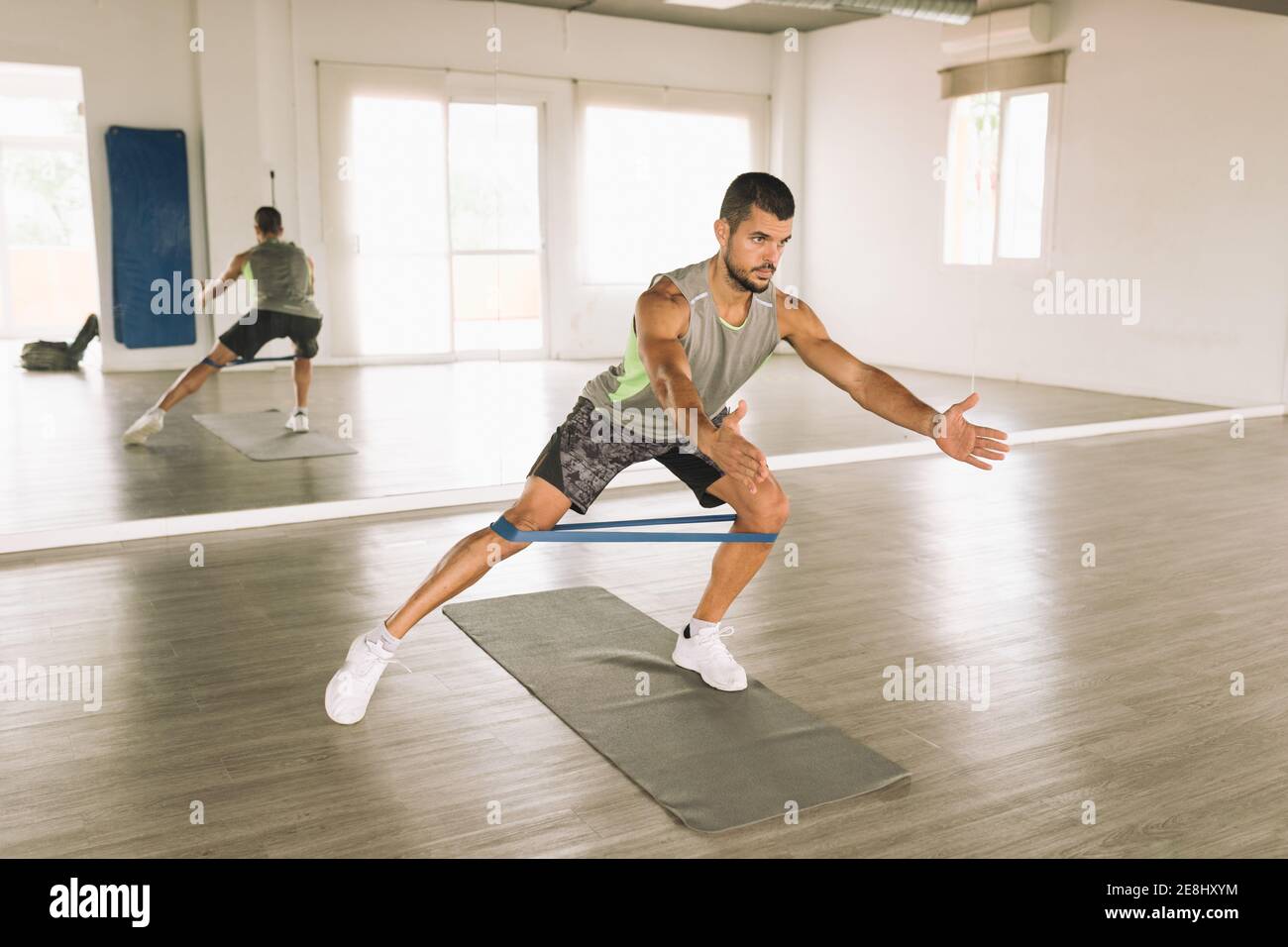 https://c8.alamy.com/comp/2E8HXYM/full-length-of-concentrated-young-athletic-guy-in-sportswear-doing-side-lunges-exercise-with-elastic-band-while-training-alone-in-spacious-fitness-stu-2E8HXYM.jpg