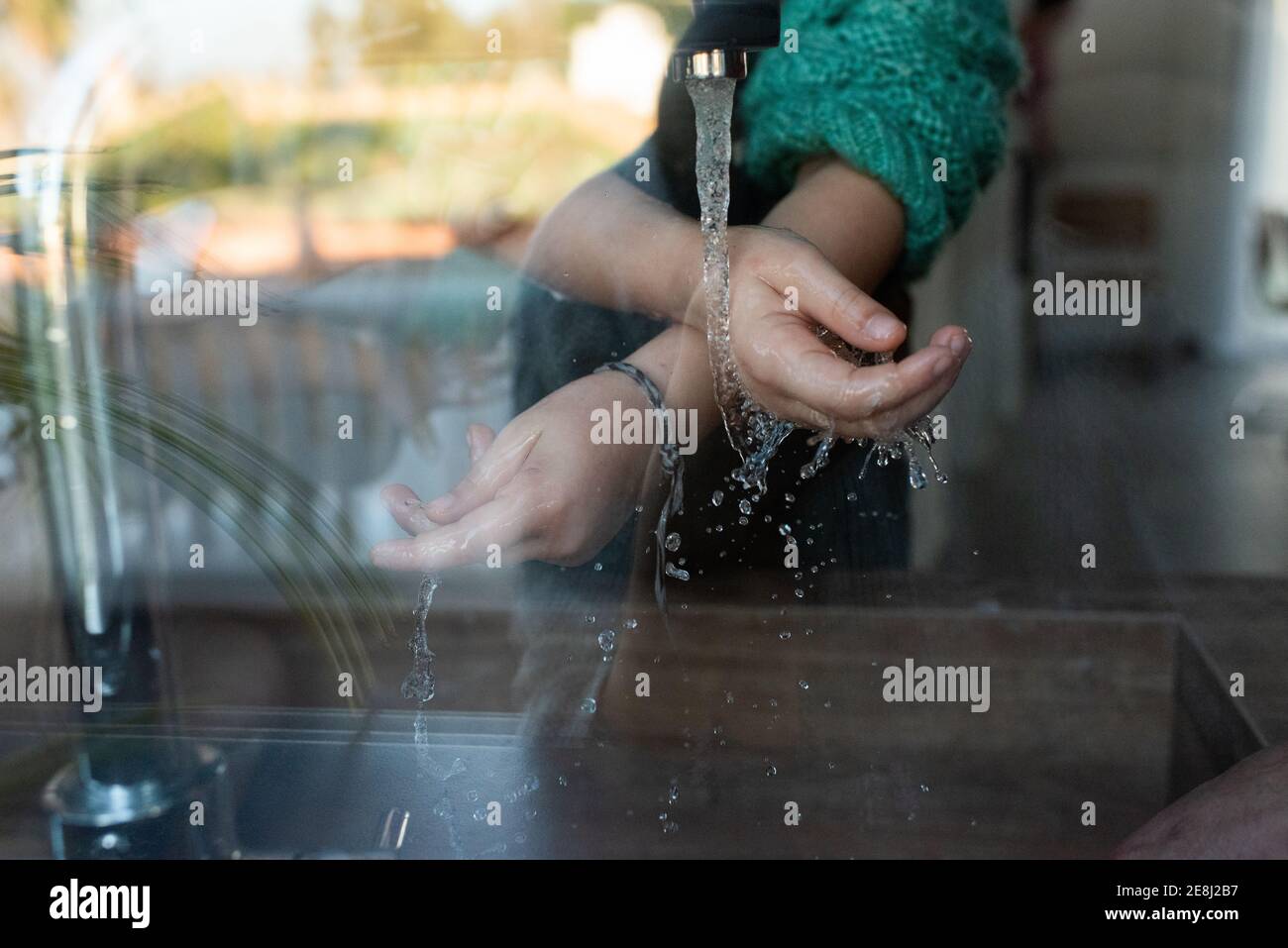Through glass of crop unrecognizable kid washing hands under running water in sink in kitchen Stock Photo