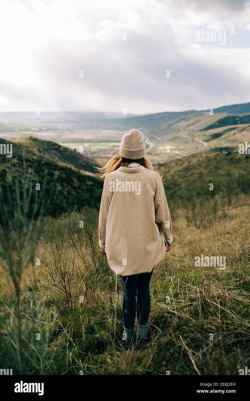 Back view of faceless tourist standing on grass while contemplating mountain under cloudy sky in Europe Stock Photo