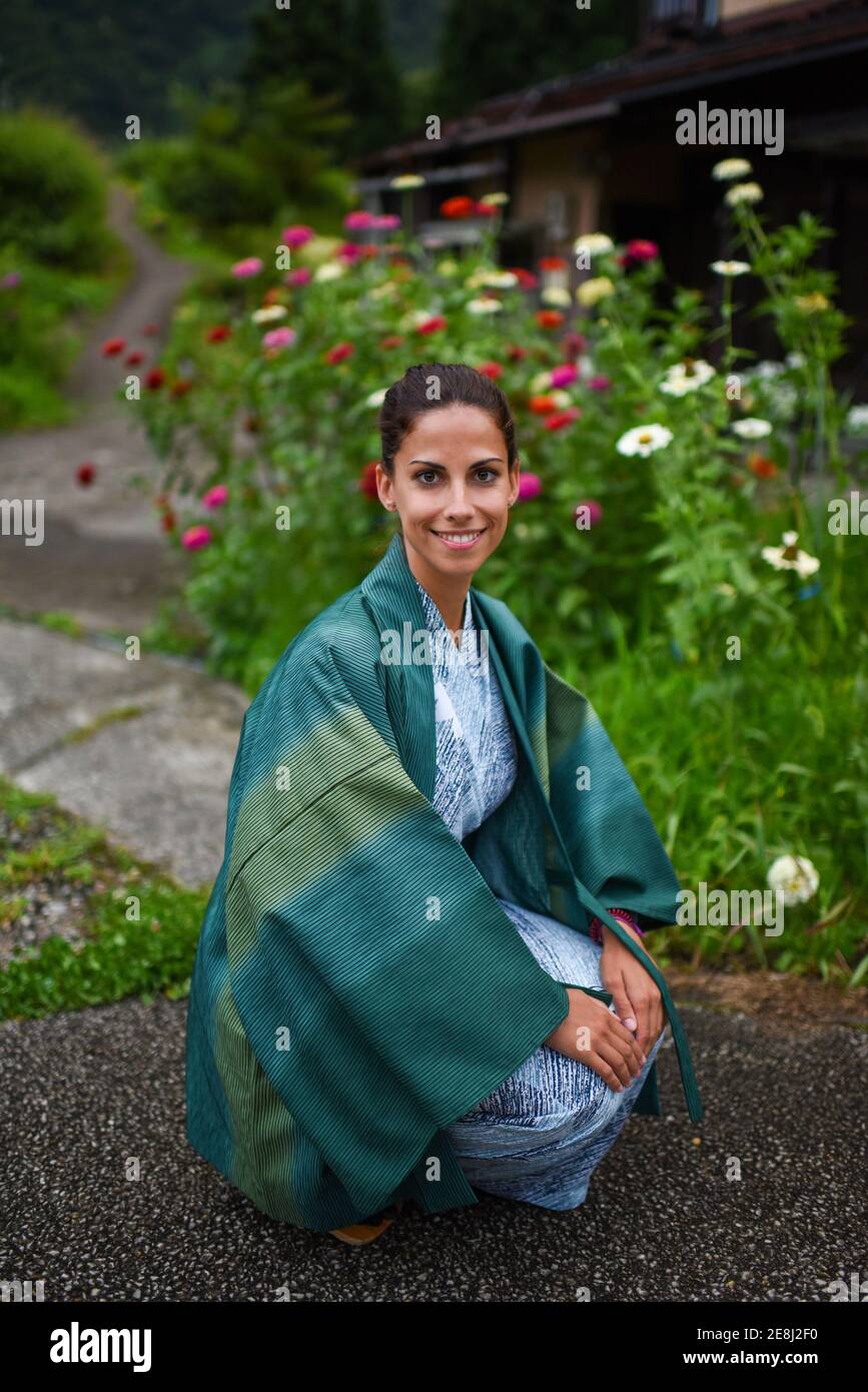Portrait of young attractive caucasian Woman in a traditional Japanese kimono surrounded by flowers in small village of Ainokura, Japan Stock Photo