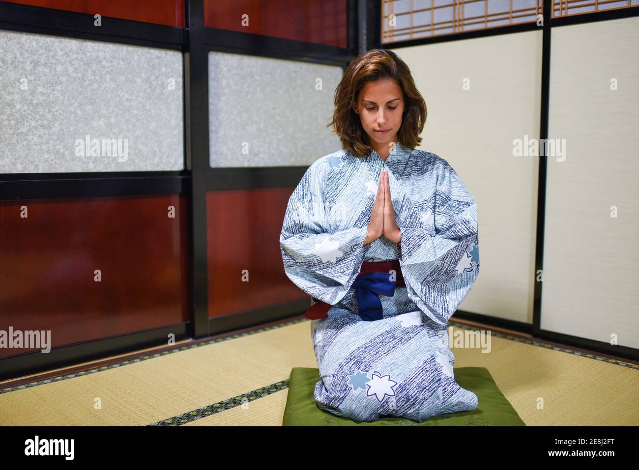 Interior portrait of kneeling young attractive caucasian Woman with hands in prayer wearing a traditional Japanese kimono inside a house, Ainokura, Ja Stock Photo
