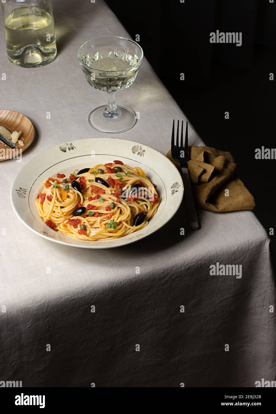 Spaghetti alla Puttanesca server with glass oh white wine placed on table with napkin Stock Photo