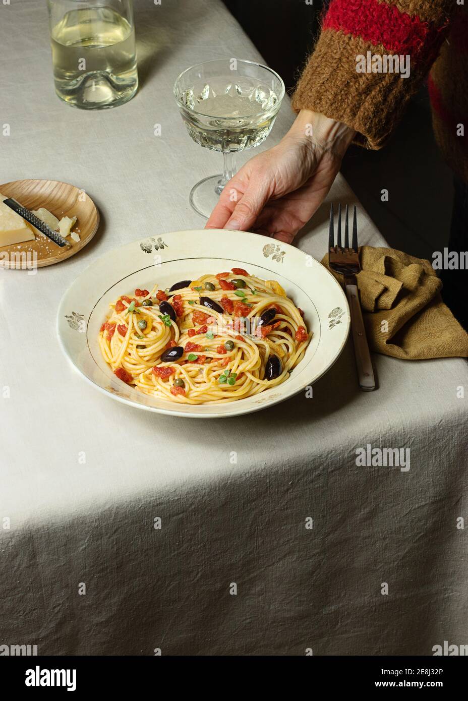 Cropped unrecognizable person eating Spaghetti alla Puttanesca server with glass oh white wine placed on table with napkin Stock Photo