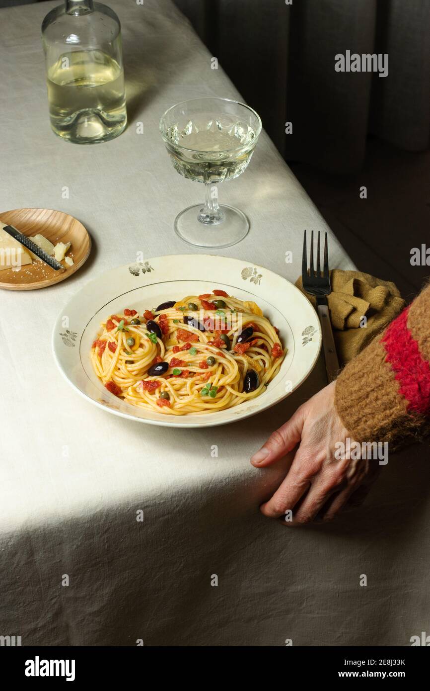Cropped unrecognizable person eating Spaghetti alla Puttanesca server with glass oh white wine placed on table with napkin Stock Photo
