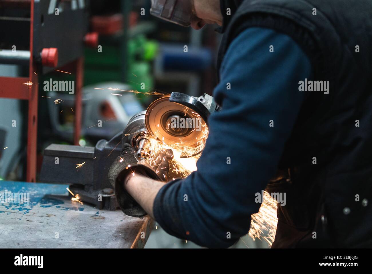 Side view of crop adult male mechanic in casual clothes and protective goggles and gloves cutting metal detail with angular grinding tool during work Stock Photo