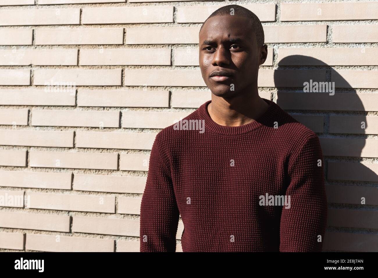 Serious young African American male standing while looking away in sunlight near billet wall Stock Photo