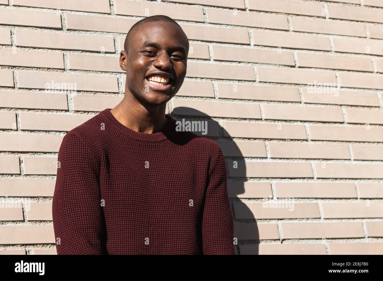 Happy young African American male standing while looking away in sunlight near billet wall Stock Photo