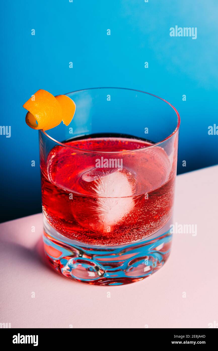 Glass of bitter alcoholic Negroni cocktail served with ice and orange peel on light surface