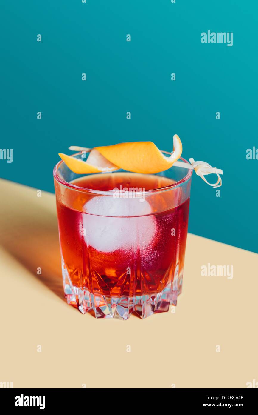 Glass of bitter alcoholic Negroni cocktail served with ice and orange peel on light surface