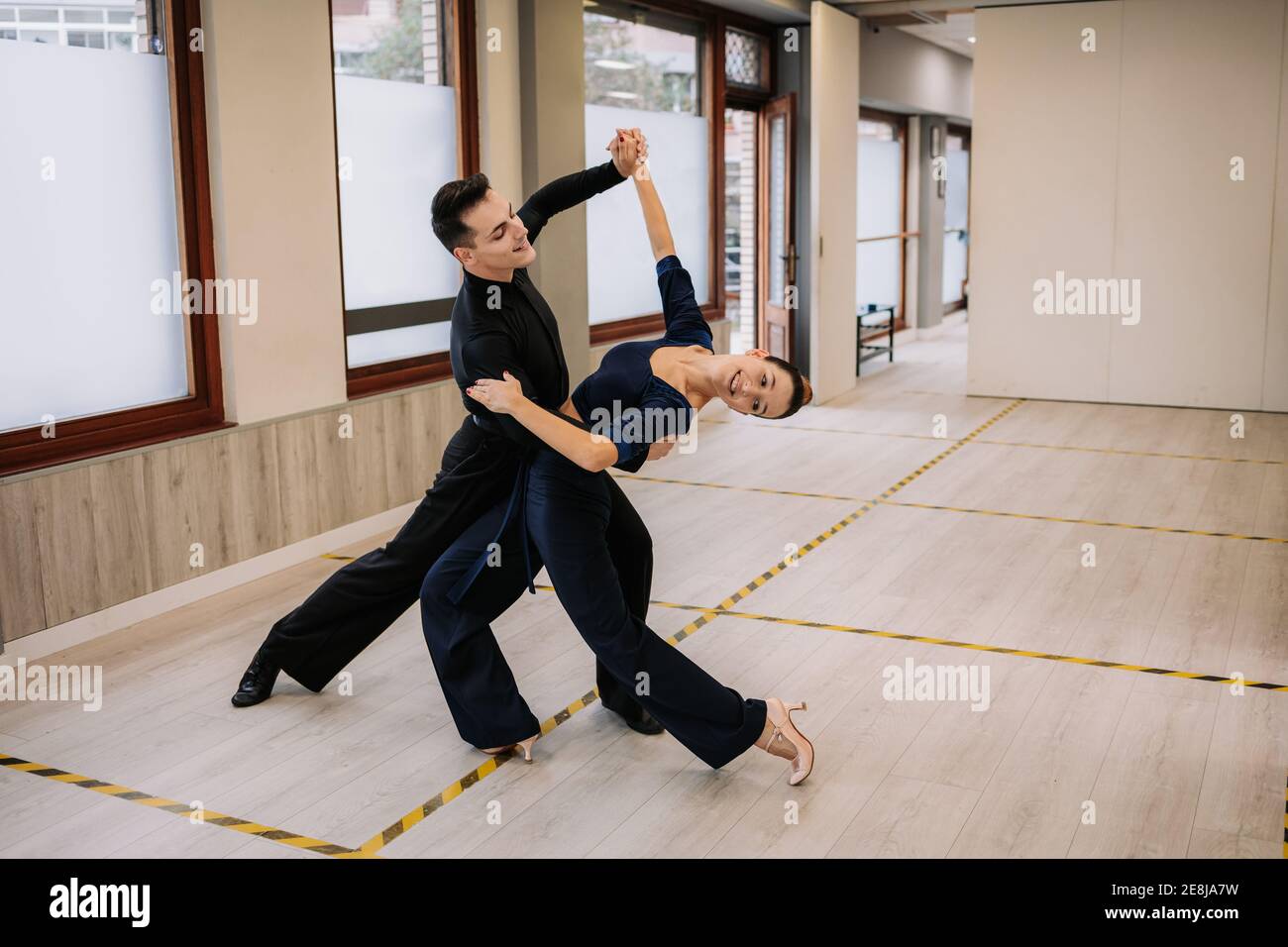 Skilled couple of dancers in elegant clothes rehearsing moves of ballroom dance during class in studio Stock Photo