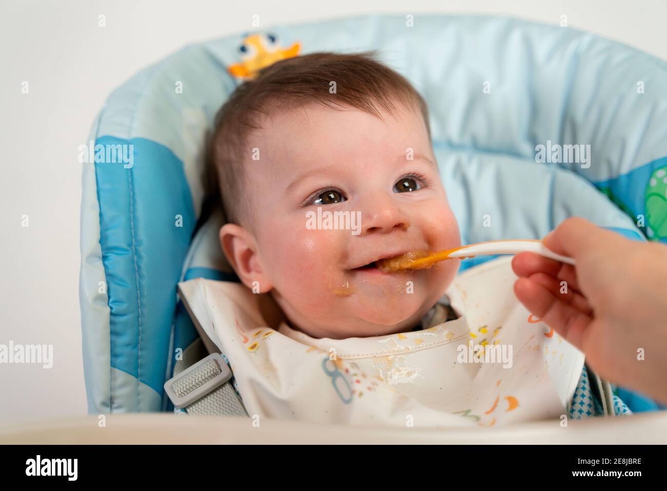 Adorable happy kid wearing bib sitting in stroller and getting fed with ...