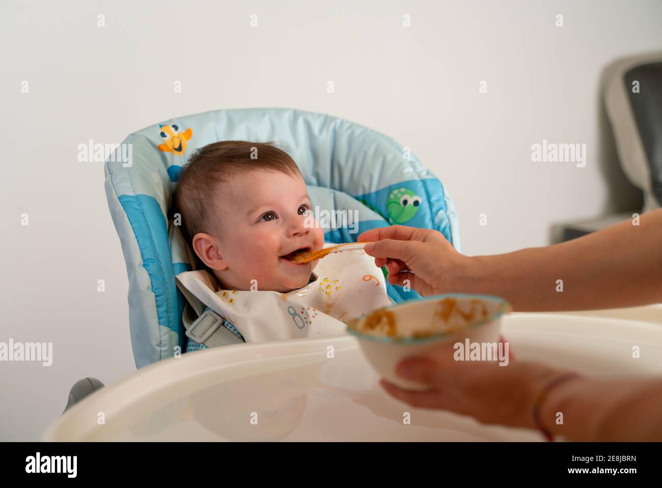 Adorable happy kid wearing bib sitting in stroller and getting fed with ...