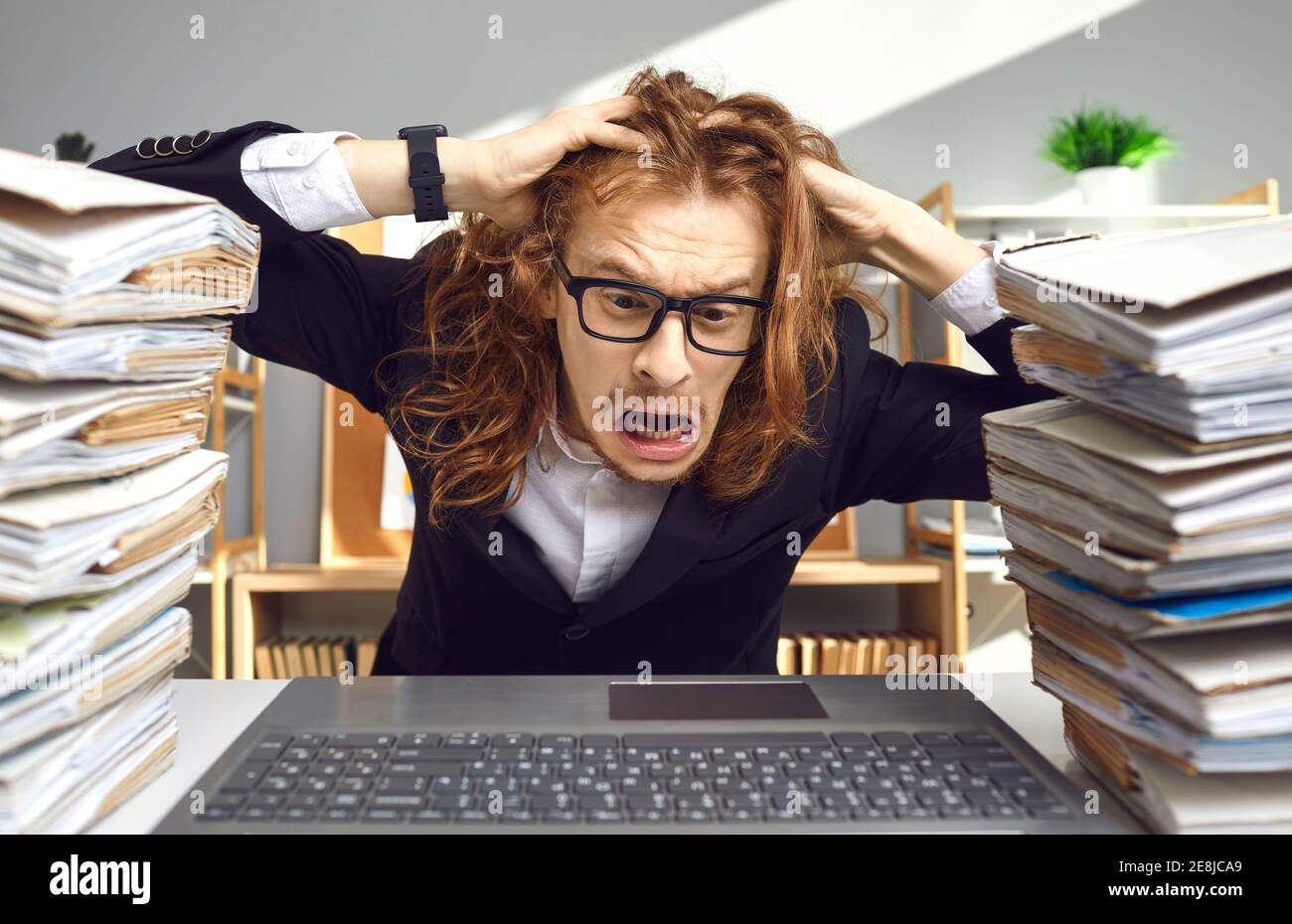 Funny man sitting at office desk with computer stressed by crazy load of paperwork Stock Photo