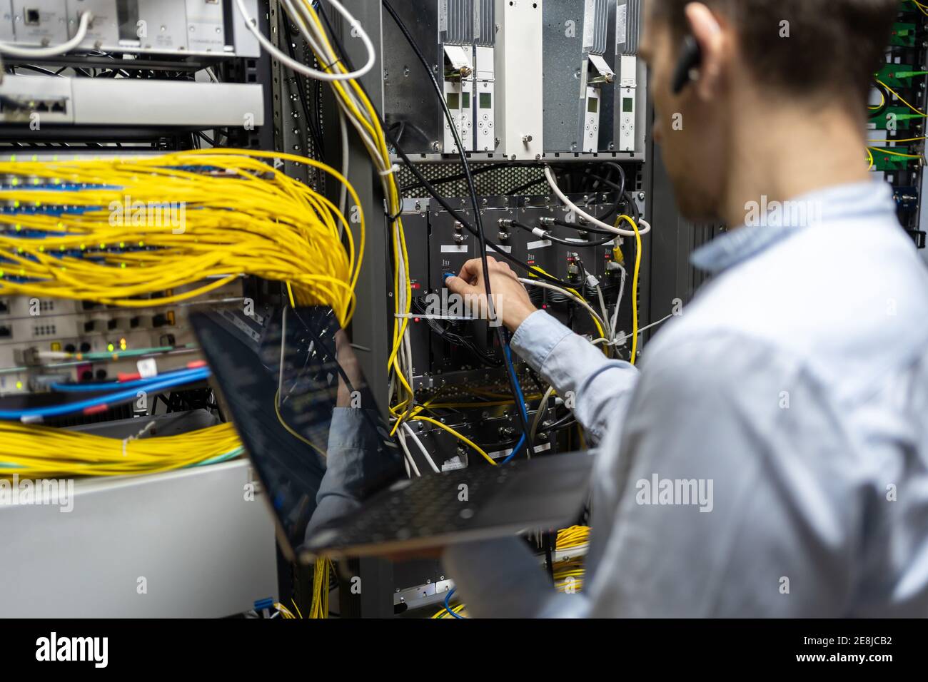Back view of crop male assistant putting cable in router while using ...