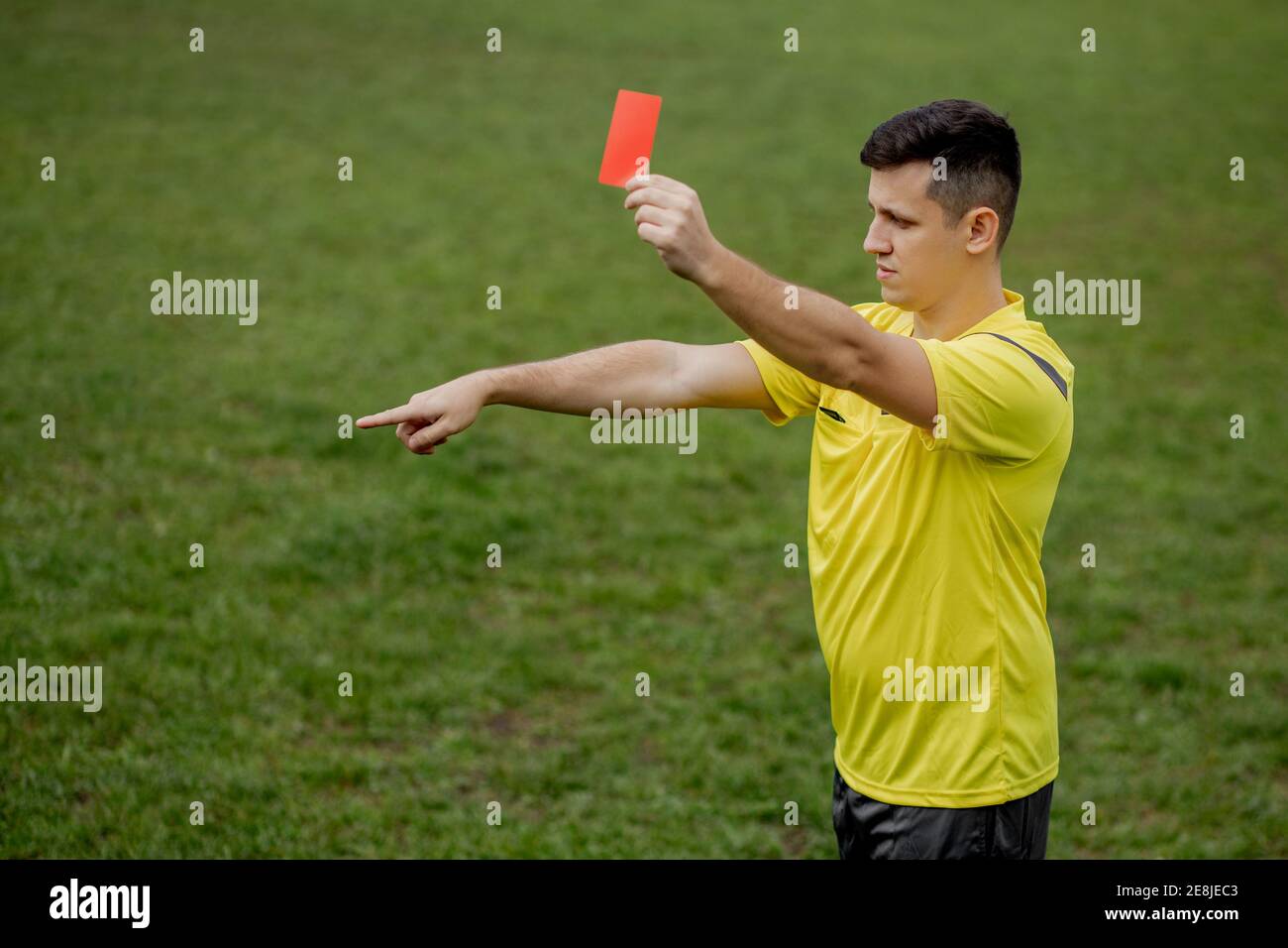 Angry football referee showing a red card and pointing with his hand on