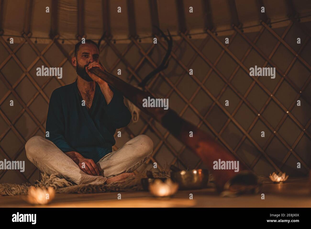 Man playng on didgeridoo by candlelight and tibetian bowl. Stock Photo