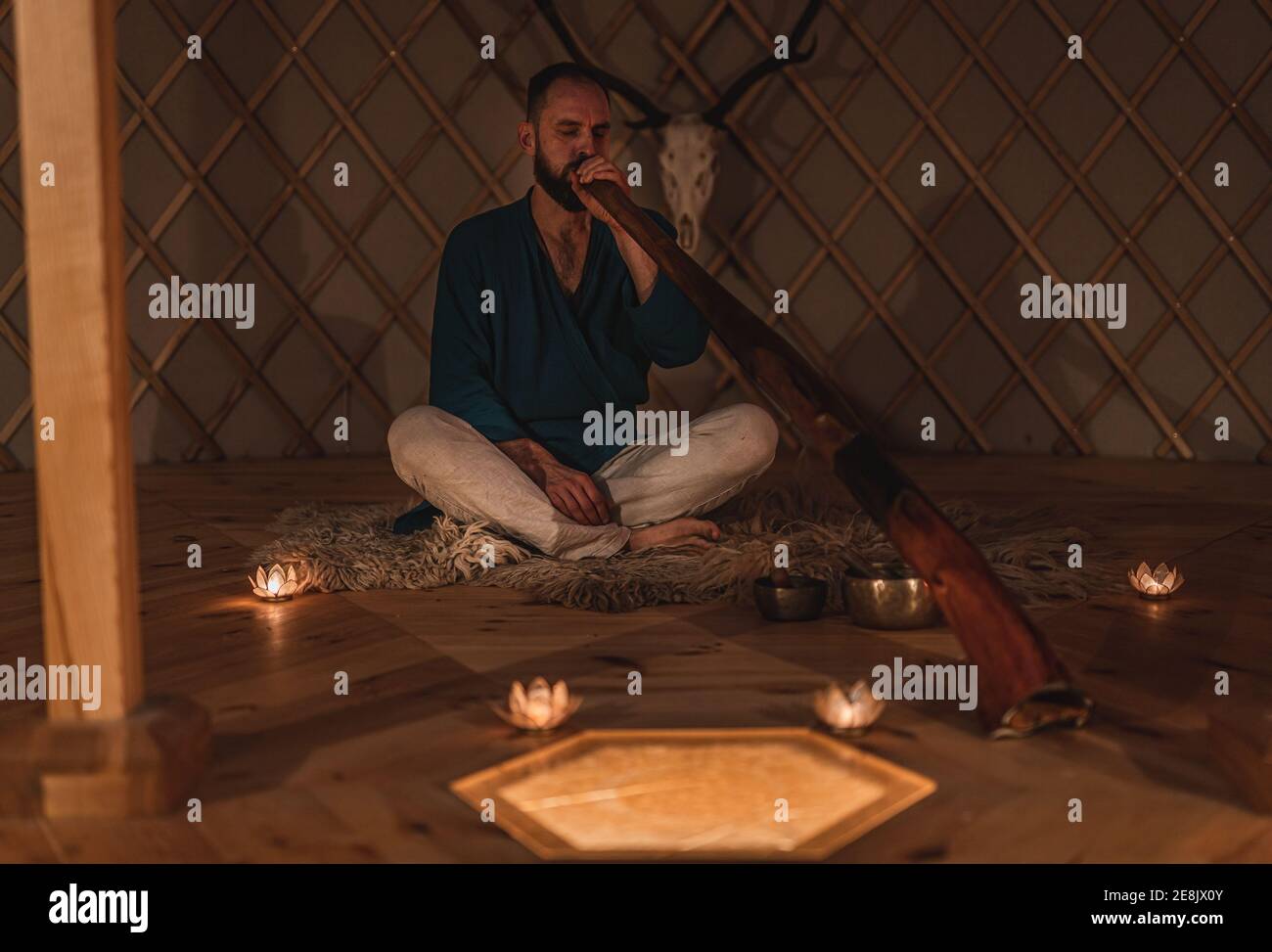 Man playng on didgeridoo by candlelight and tibetian bowl. Stock Photo