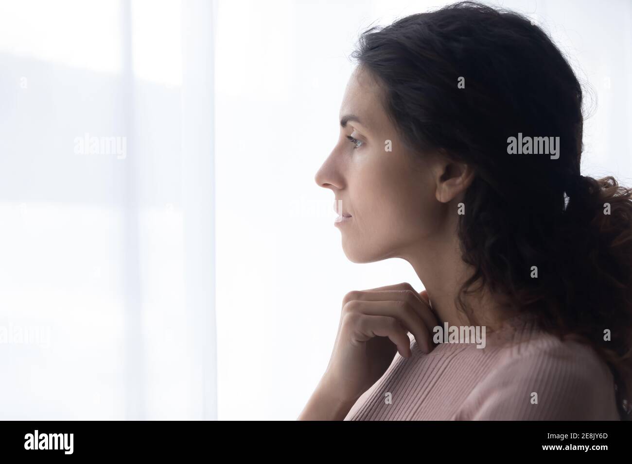 Thoughtful young caucasian woman standing near window. Stock Photo