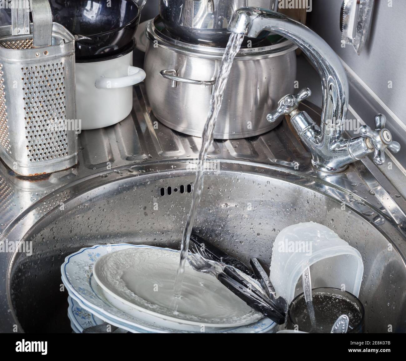 Jet of water pours from the tap onto dirty dishes in kitchen sink Stock