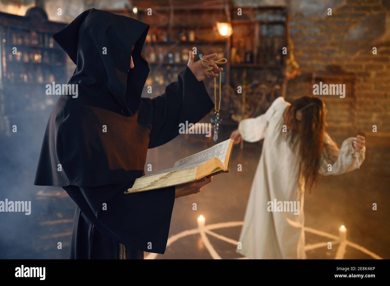 Exorcist in hood casting out demons from a woman Stock Photo