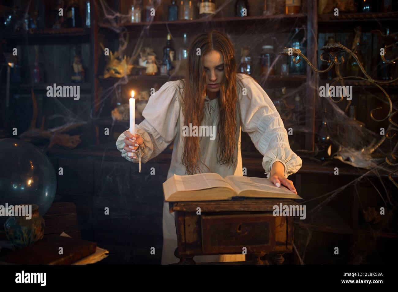 Demonic woman with candle reads book of spells Stock Photo