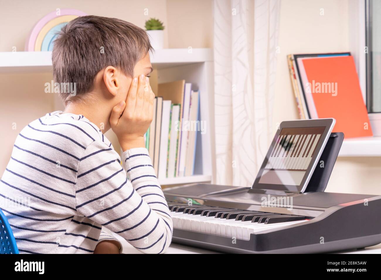 Teenage boy watching video lesson at tablet computer and learing playing digital piano at home. Online learning remote education Stock Photo