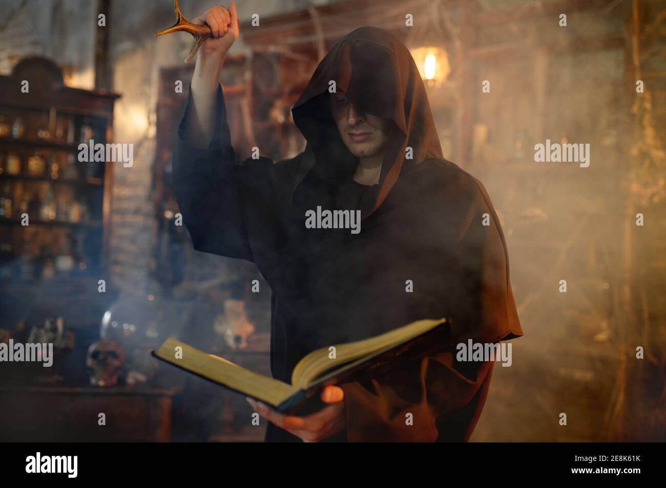 Male exorcist in black hood holds book of spells Stock Photo
