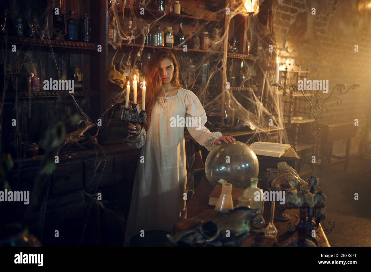 Scary woman with candle standing near the potions Stock Photo