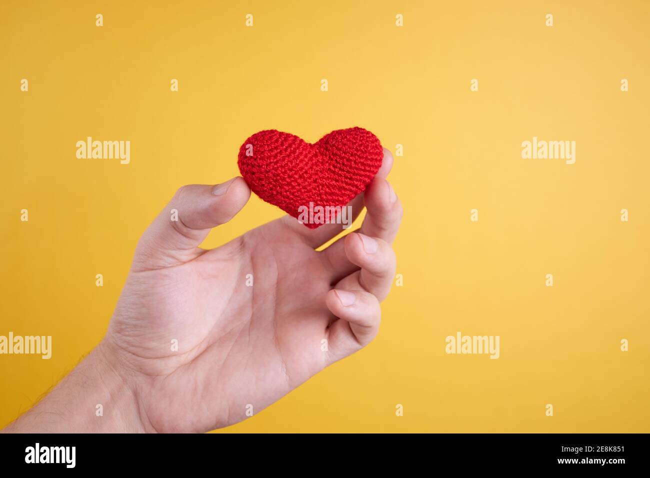 male person hold heart at his hand isolated on yellow background. romance and valentine day concept Stock Photo