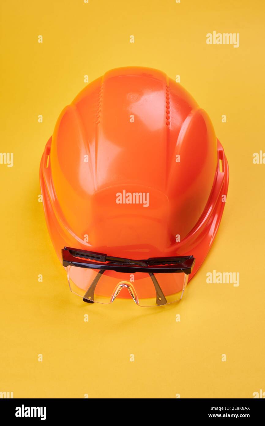 orange protective helmet and safety glasses near it on a bright yellow background. protective workwear and construction industry concept Stock Photo